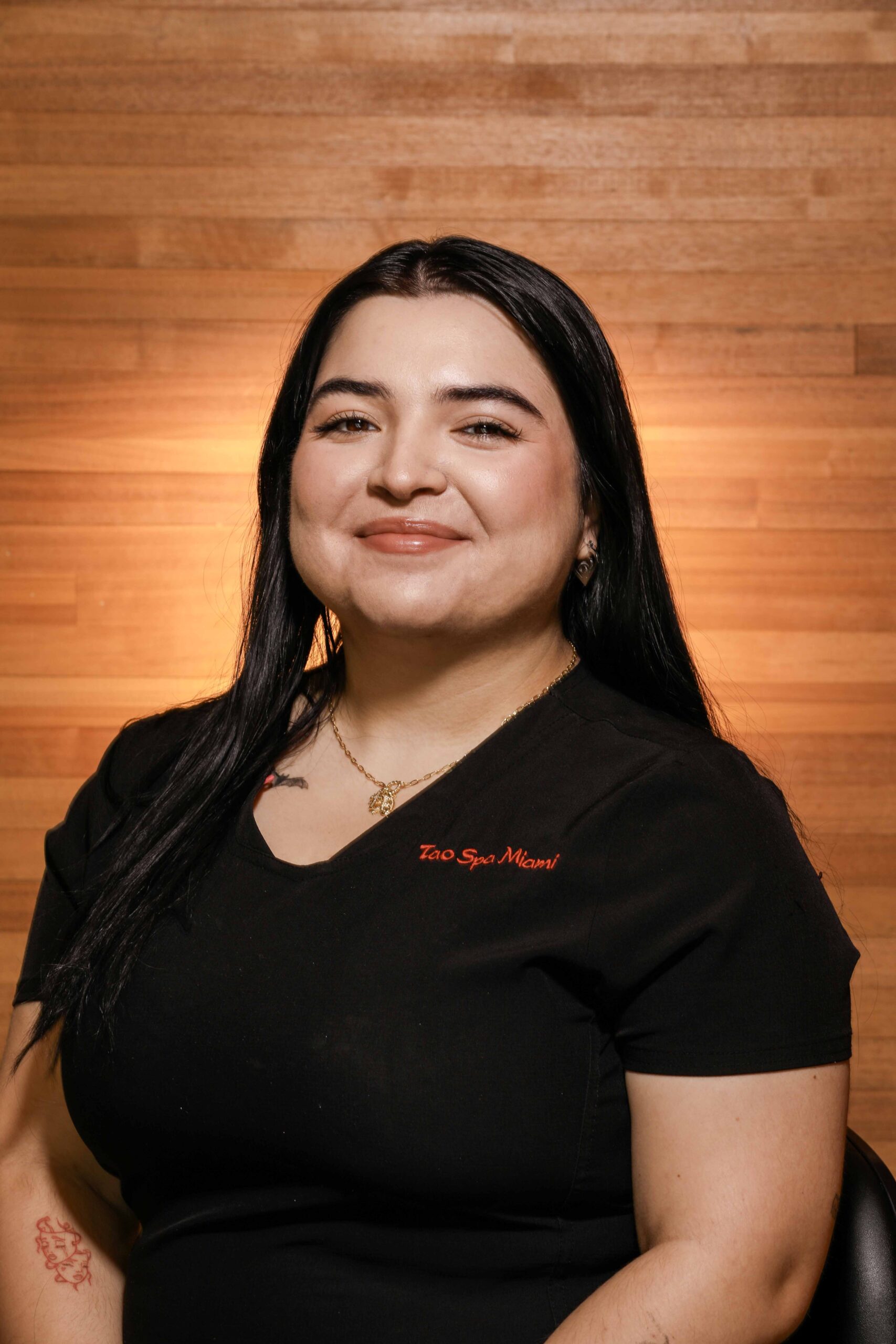 Woman smiling in spa uniform, warm background.